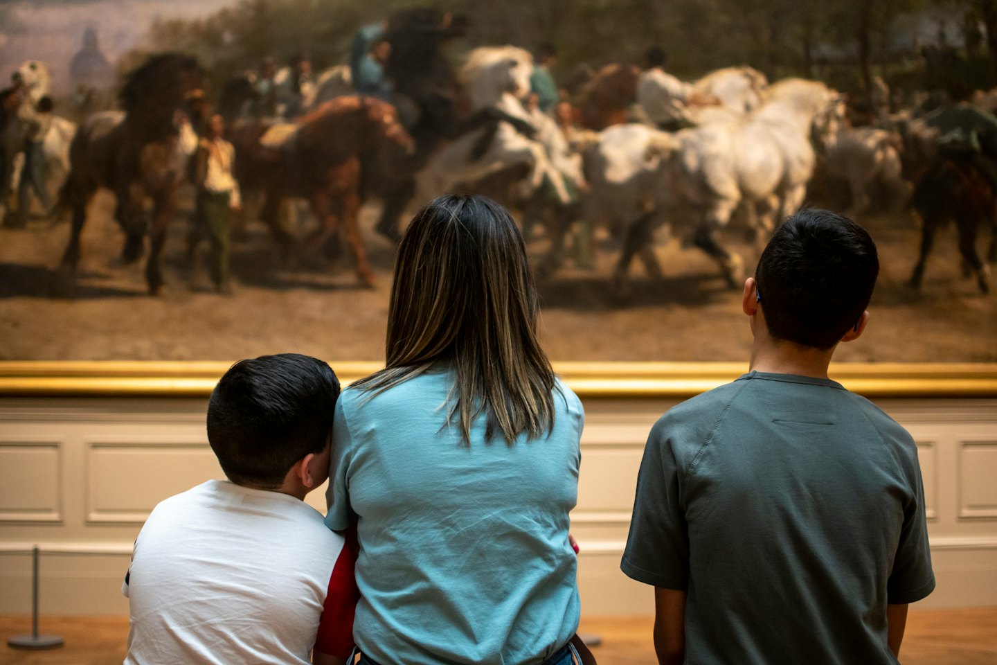 Tre persone in piedi guardano un dipinto classico in una galleria.