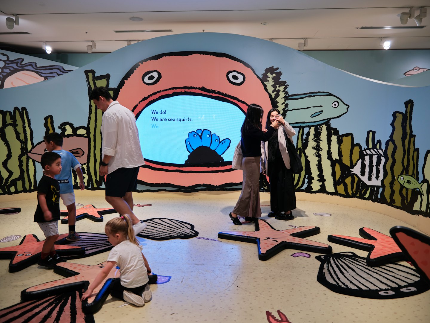 Famiglie esplorano una mostra per bambini a tema marino con installazioni interattive.