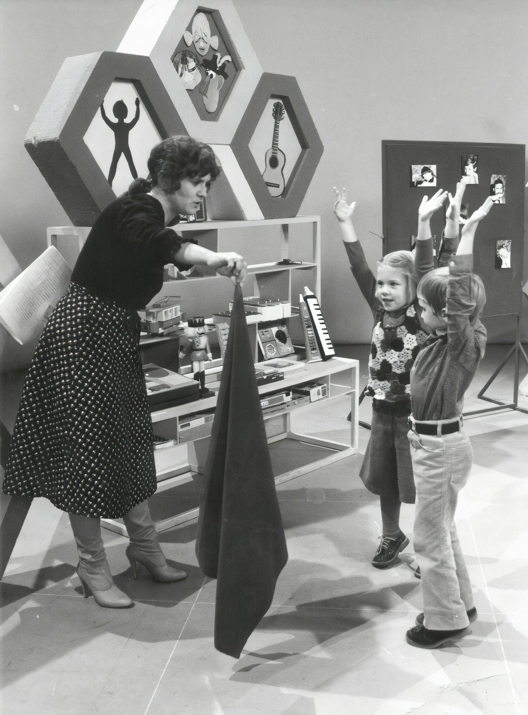 Una presentatrice mostra un tessuto a due bambini entusiasti in uno studio.