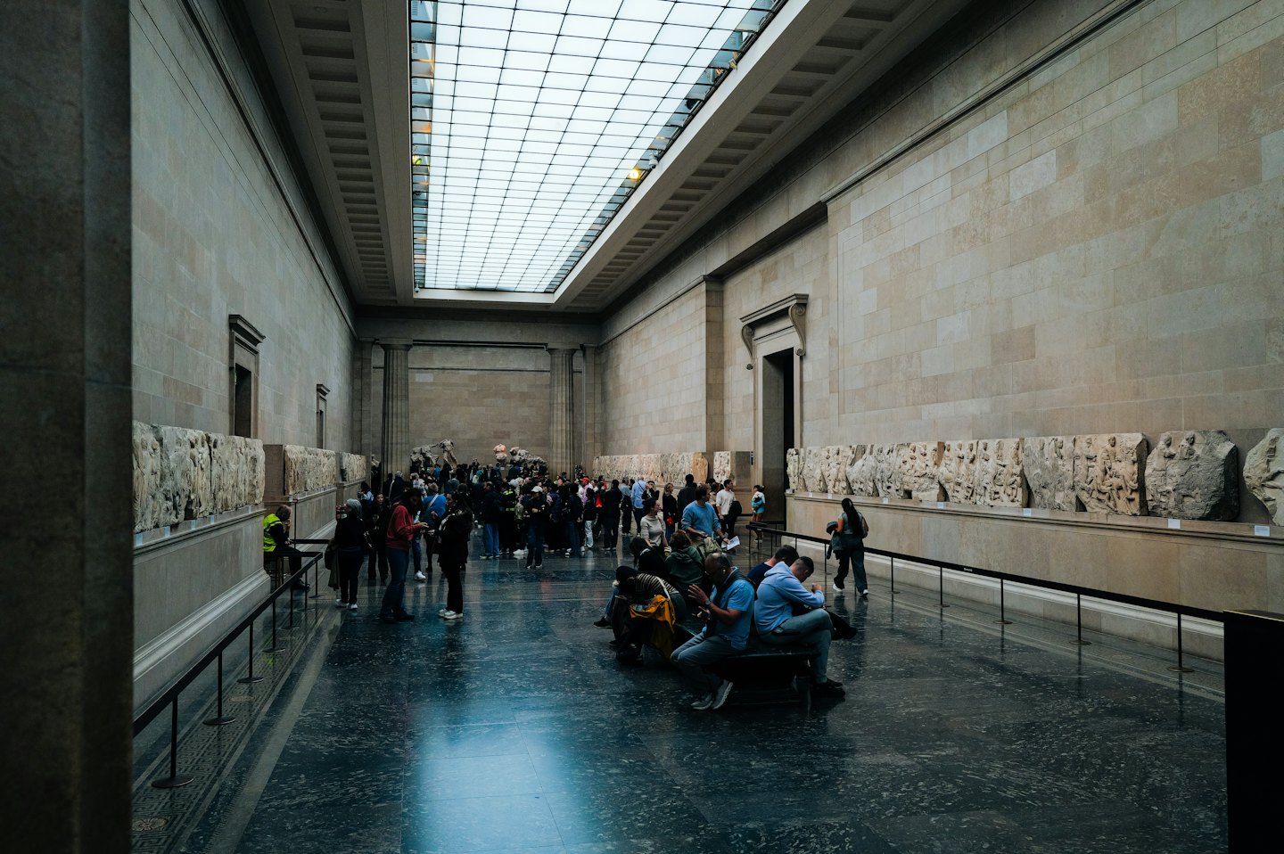 Visitatori che esplorano un'ampia sala museale con sculture e bassorilievi.