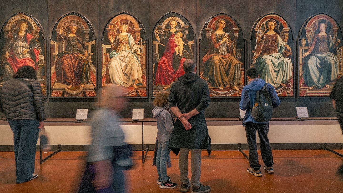Visitatori osservano grandi dipinti classici in una galleria museale.